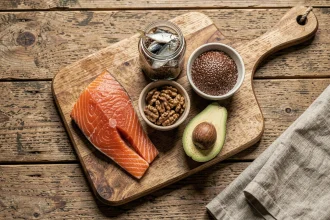 Sélection d'aliments riches en oméga 3 disposés sur une planche en bois rustique : saumon cru, noix, graines de lin, avocat et sardines