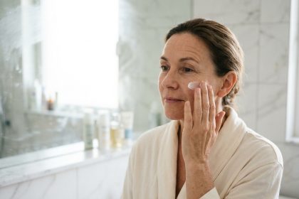 Femme de 40 ans appliquant une crème de jour anti-âge sur son visage devant un miroir de salle de bain