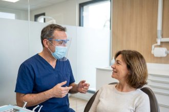 Dentiste en blouse bleue parlant à une patiente dans un cabinet moderne