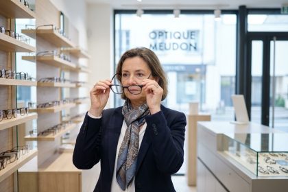 Femme en tenue d'affaires examinant des montures de lunettes dans un magasin moderne
